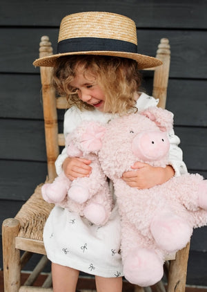 Child sitting on a wooden chair holding pink plush soft toy pigs against a dark wooden background