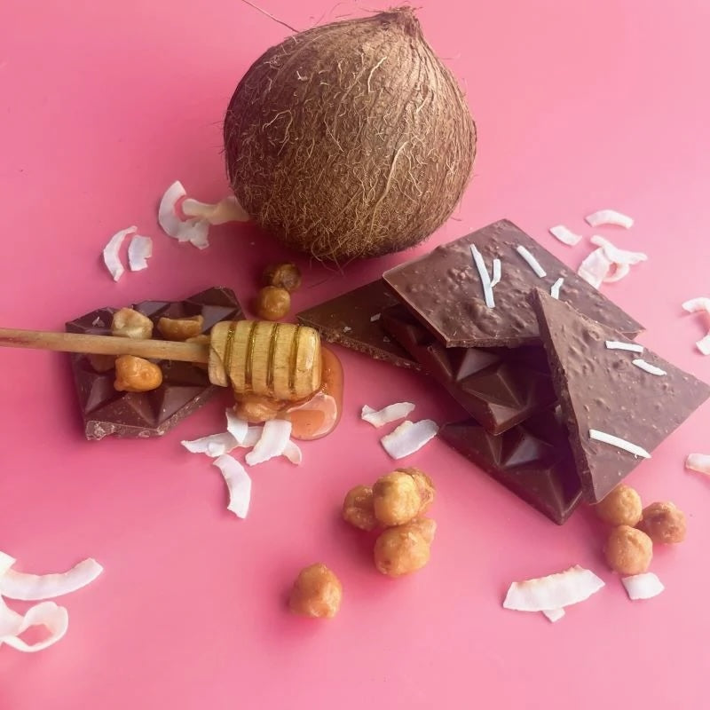 Chocolate bar with coconut pieces next to its packaging on a white background