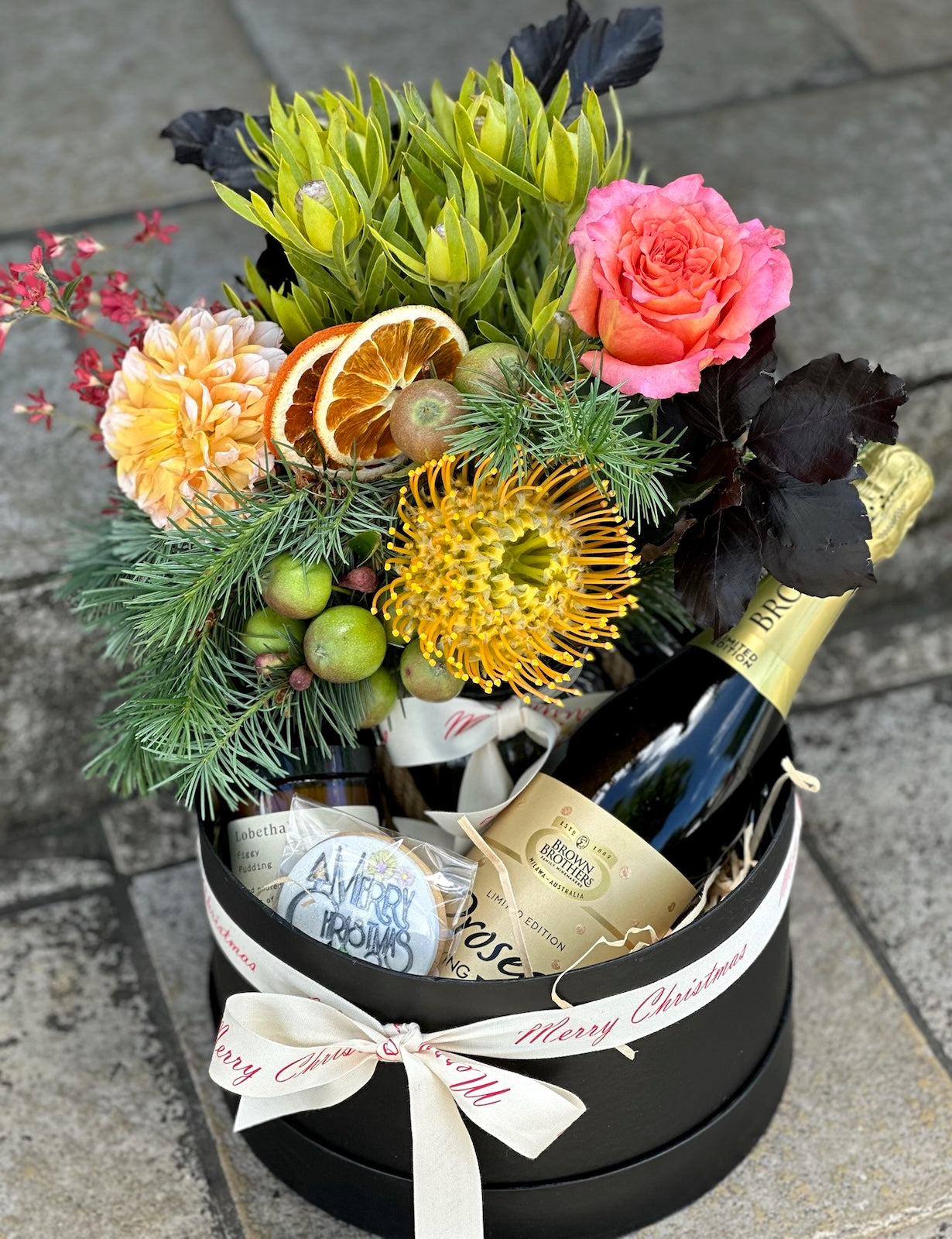 Hamper with a selection of sparkling wine, flowers in a vase, cookie and candle, in a lovely gift box.