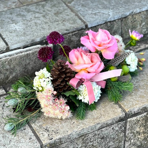 Table arrangement of flowers with pink roses, greenery, and a pink ribbon on a stone surface.