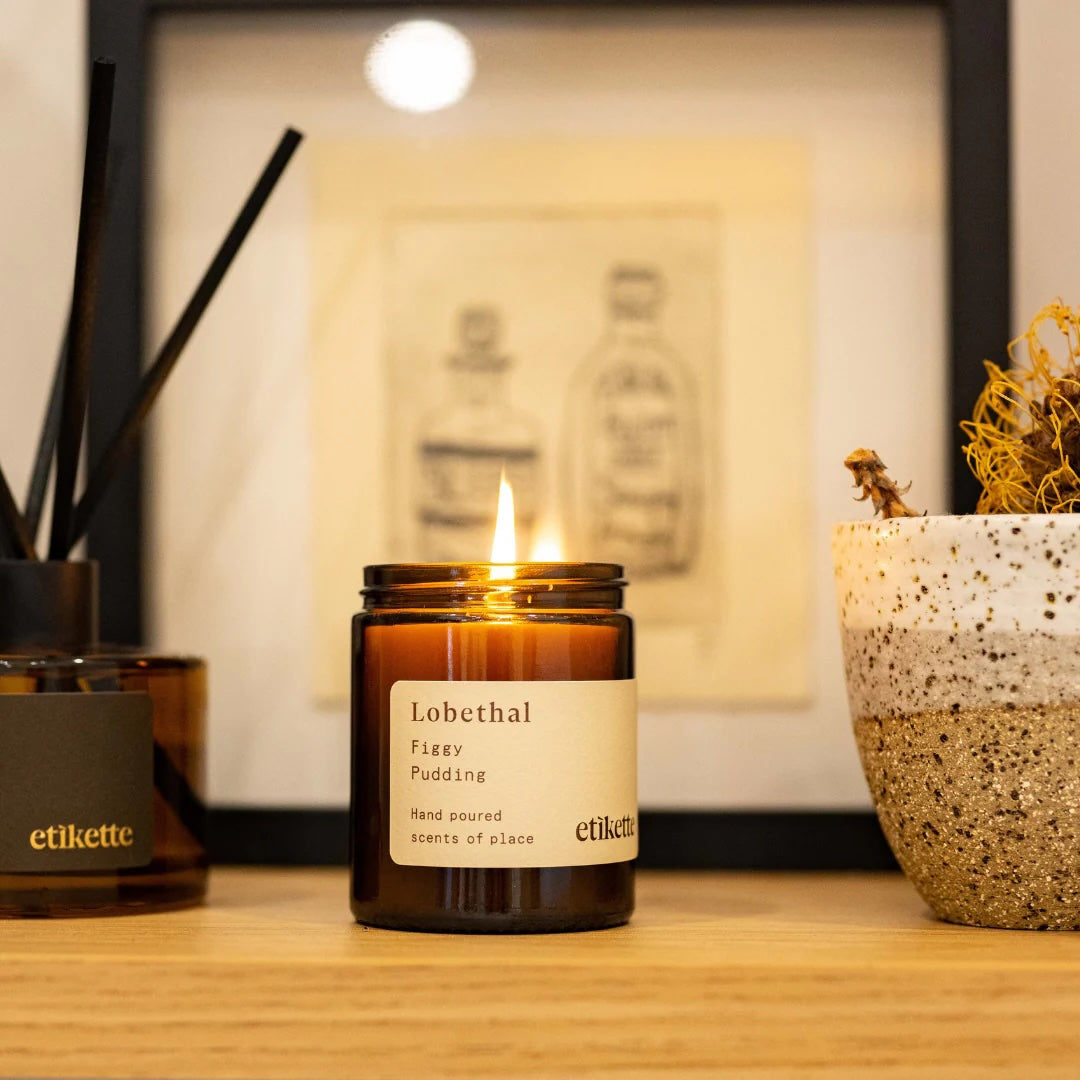 Christmas candle in a glass jar on a wooden surface with plants around the candle.