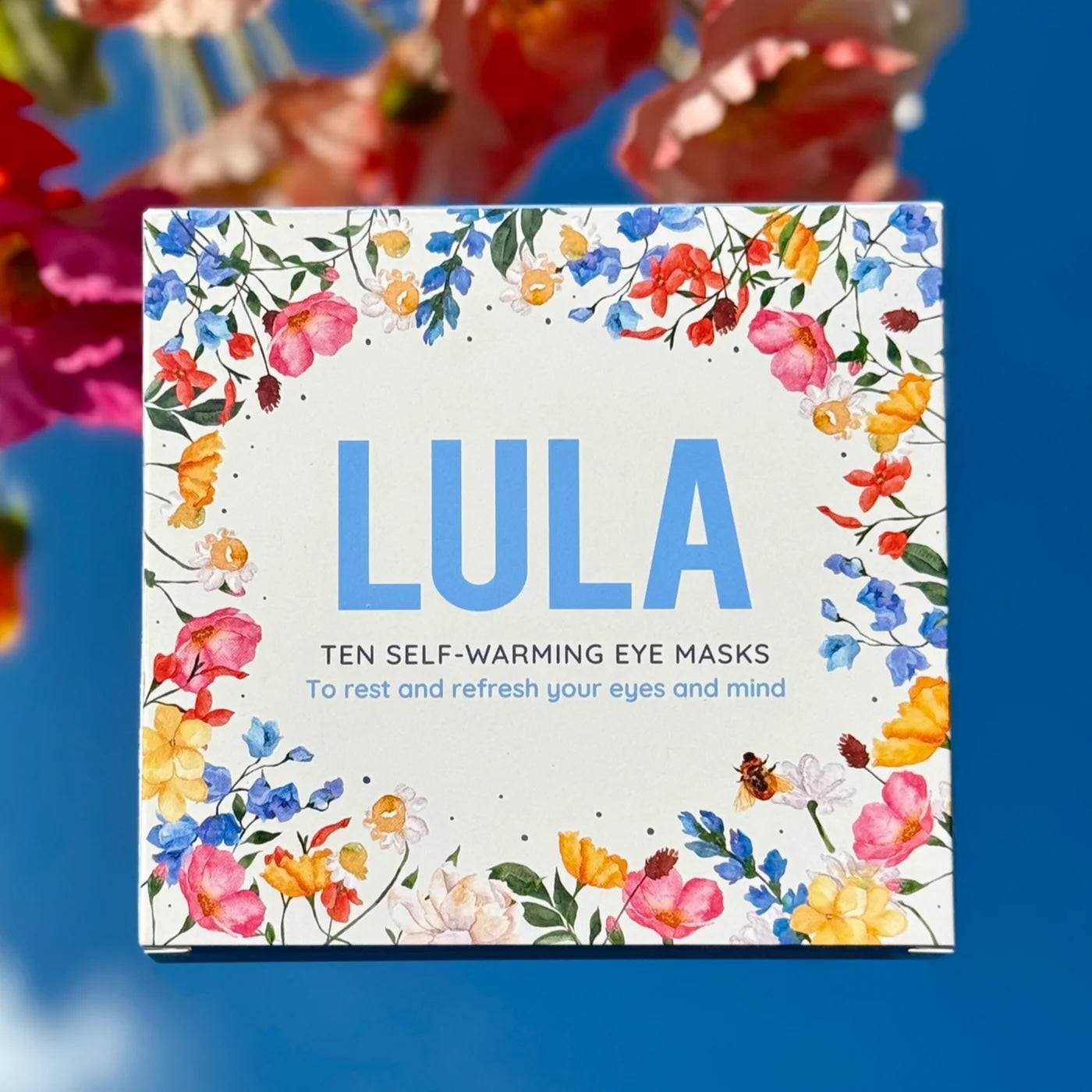 Self-warming eye masks packaging with floral design on a blue background.