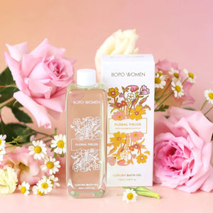 Floral fields luxury bath oil bottle and decorative packaging with roses and daisies on a pink background
