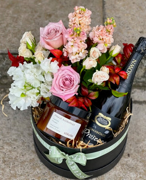 A gift box filled with flowers, candle and prosecco wine.