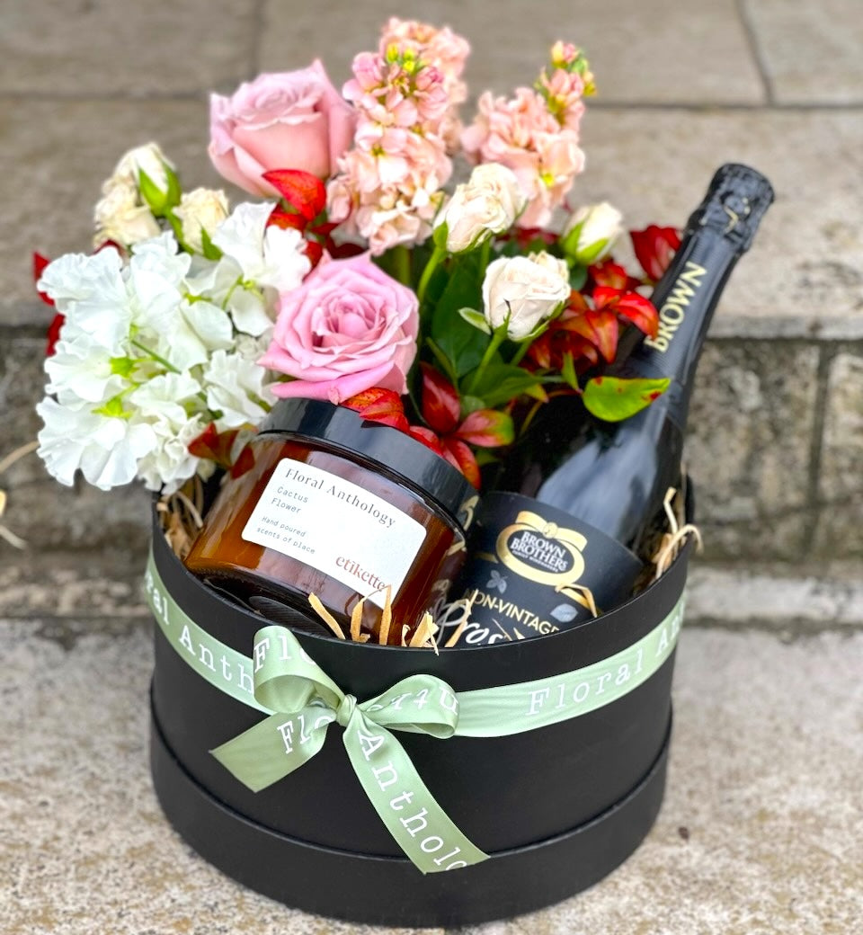 A gift box filled with flowers, candle and sparkling wine