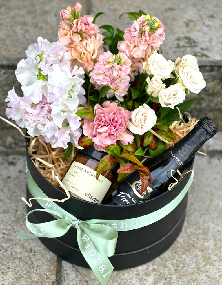 A gift box filled with flowers, candle and sparkling wine