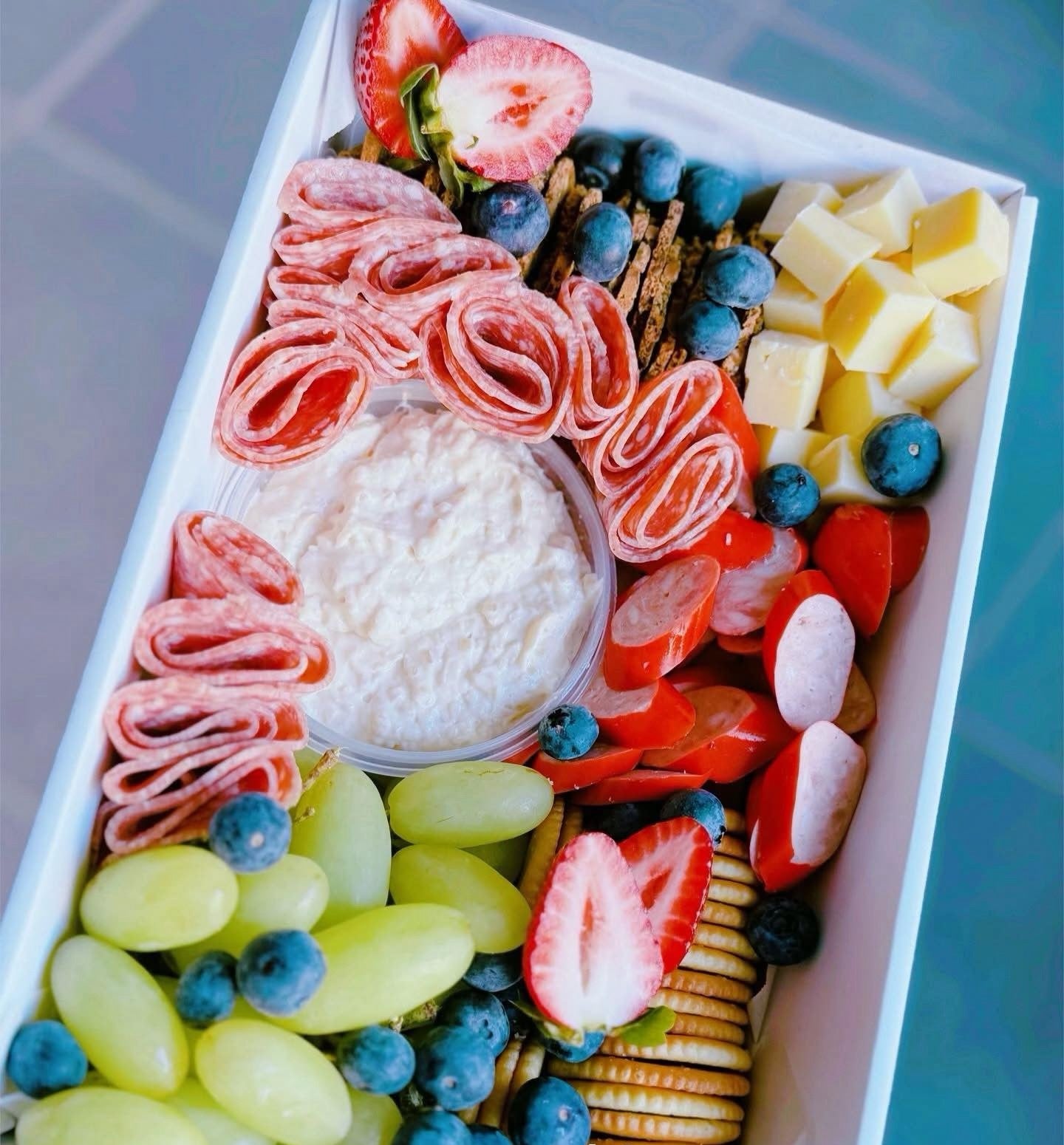 Platter of assorted meats, cheeses, and fruits on a white tray with a green background.