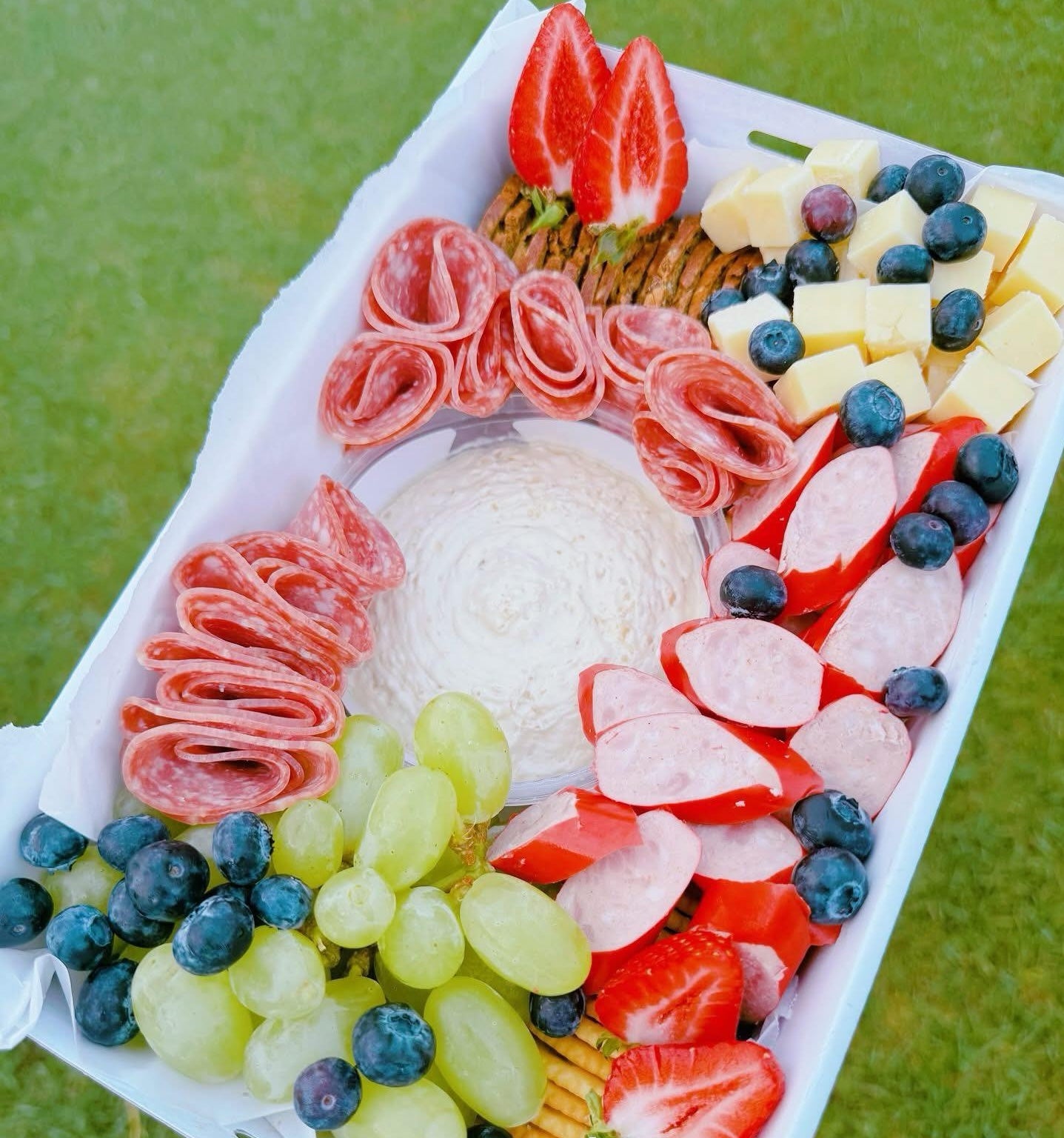 Platter of assorted meats, cheeses, and fruits on a white tray with a green background.