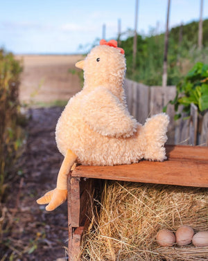 Plush chicken toy on a wooden platform with hay and eggs in an outdoor setting