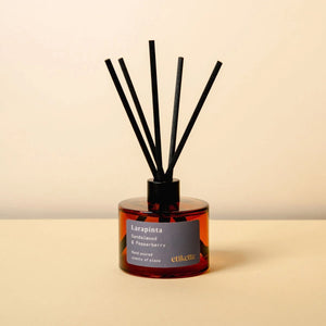Reed diffuser reading 'Larapinta sandalwood and pepperberry scent' with black sticks in a amber bottle on a beige background