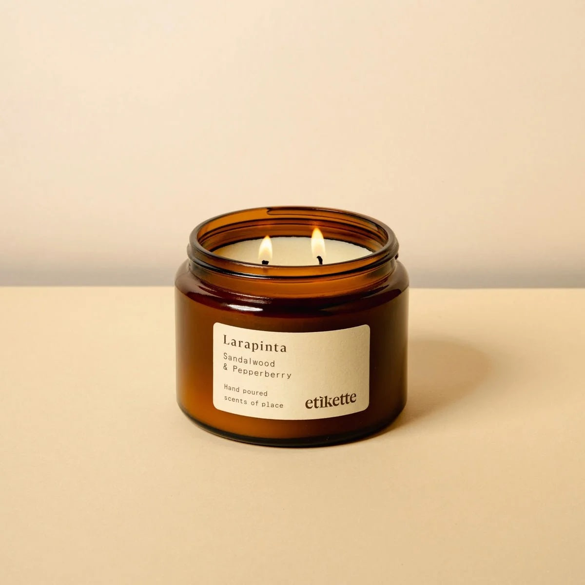 Double wick soy candle in an amber jar with a label reading Larapinta sandalwood and pepper berry, on a beige background