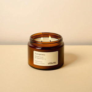 Double wick soy candle in an amber jar with a label reading Larapinta sandalwood and pepper berry, on a beige background