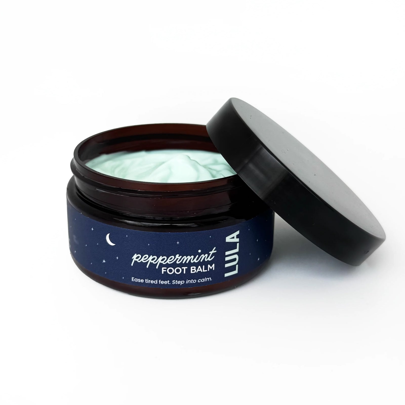 Open jar of peppermint foot balm with a black lid on a white background