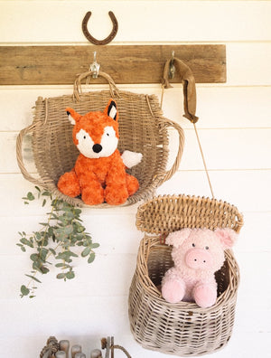 Wicker baskets with plush soft toy pig and fox on a wooden wall.