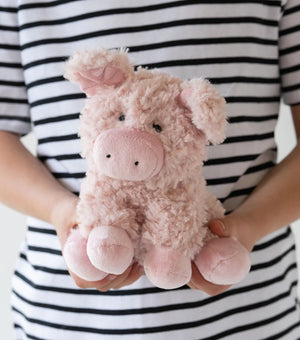 Girl holding a pink plush soft toy in the shape of a pig, against a striped background